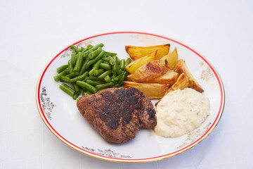 Beef steak from sirloin served on white vintage porcelain plate with roasted potatoes or chips steamed green beans and tartar sauce isolated on white background. Delicious and balanced lunch or diner