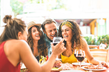 Group of people having fun drinking red wine and dining together sitting outside restaurant terrace-Young friends laughing and enjoying happy hour at pub- Lifestyle Food and beverage concept - obrazy, fototapety, plakaty
