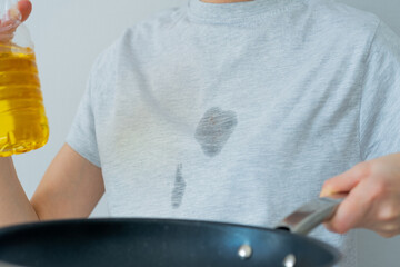 Grease stains in a clothes. An unrecognized woman is holding a corn oil and a frying pan in the...