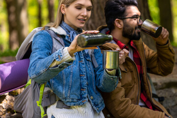 Two travelers drinking tea from metal cups after a long walk