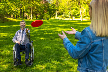 Man on a wheelchair and his wife playing frisbee and loking contented