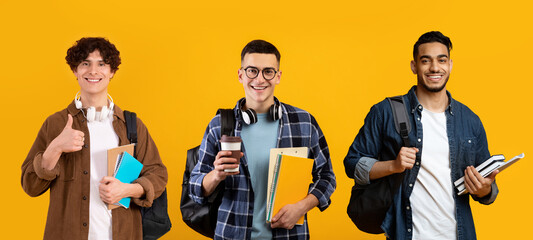 Three happy male students carrying backpacks and workbooks posing over yellow background
