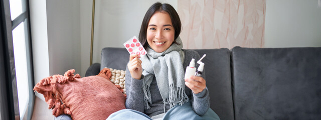 Portrait of happy smiling asian girl showing medication, sore throat spray and drugs from flu or...