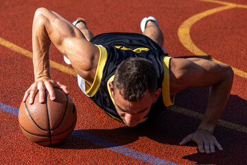 Man doing push ups with a basketball ball workout outdoor on basketball court.