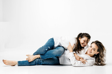 Obraz na płótnie Canvas Young mother and little girl playing on a white background. The concept of advertising positive, happy sincere emotions, clothes and a happy carefree life.
