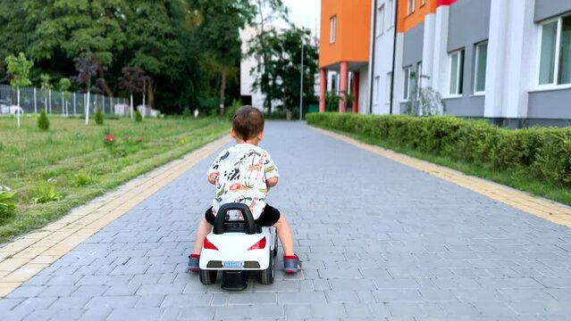 Rear view of a baby boy driving a toy car outdoors. Kid quickly moves his feet to push from the ground and ride.