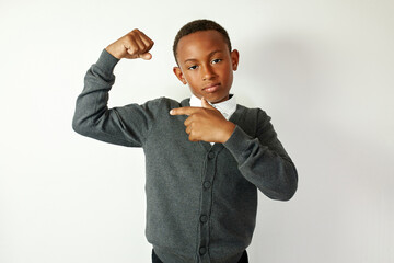 Portrait of serious cool confident african american kid posing against white studio background with arrogant facial expression bragging with bicep, showing off, pointing at his arm, feeling powerful