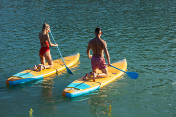 Woman and man surfing in ocean on sup board ar summer vacation.
