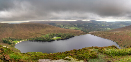 Panoramic view on lake Lough Bray with house, small forest and beach, surrounded by dramatic storm...