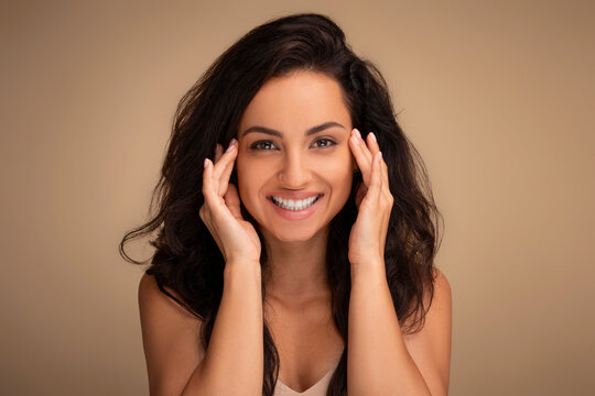 Smiling attractive brunette long-haired young woman touching face skin temples