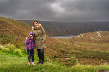 Mother and daughter standing and looking at camera, Lough Bray surrounded by storm clouds in...