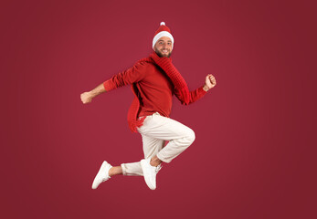 Smiling millennial caucasian guy in Santa hat jumps, frozen in air, enjoy holidays