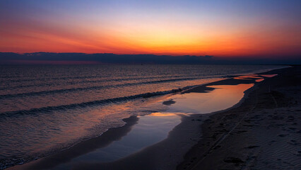 Sunset panorama with orange sky and reflection on the beach and water. Mediterranean, Camargue, Gard, France.