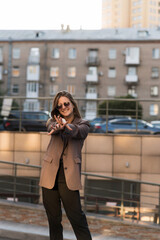 Fototapeta premium Portrait of a Caucasian attractive and happy young woman in casual clothes and sunglasses in the city while walking on a sunny day. The concept of style, fashion, youth and lifestyle