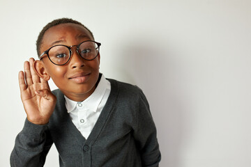 Studio portrait of schoolboy in glasses eavesdropping holding hand around right ear, wearing funny...