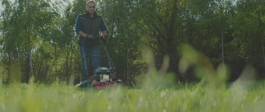 Low angel view of a man pushing lawnmower through small backyard in spring. Shot in slow-motion