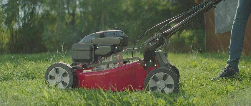 Electric Lawn Mower Being Started And Pushed Forward For Cutting Green Grass At Backyard. Low Angle Shot