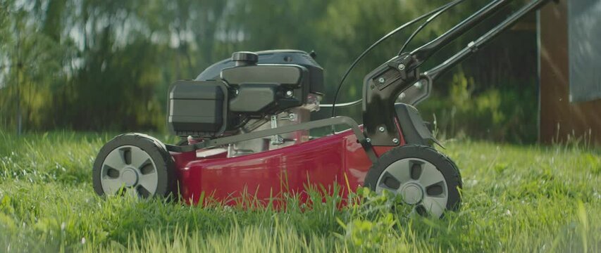 Side view of a man starting a lawnmower in his garden and pushing it forward for cutting green grass. Shot in slow-motion