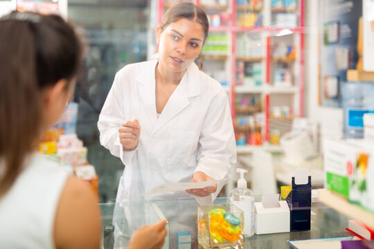 Female Pharmacist In Mask Standing Behind Counter And Talking With Buyer