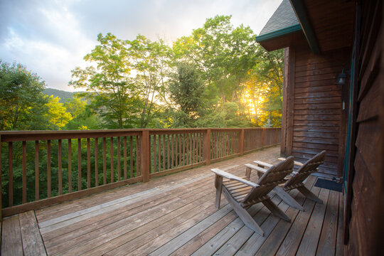 Two wooden adirondack chairs on cabin porch facing the forest overlook