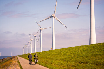 people driving bicycle on road close to wind turbines