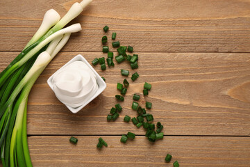 Bowl of tasty sour cream and sliced green onion on wooden background