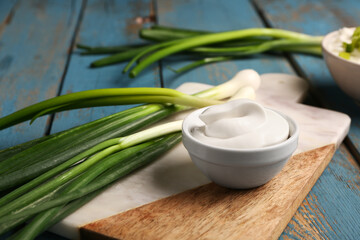 Board with bowls of tasty sour cream and green onion on blue wooden background