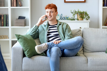 Young redhead man talking by mobile phone on sofa at home