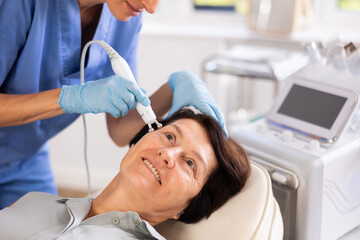 Mature female client receiving hardware ultrasonic to revitalize and tighten facial skin at...