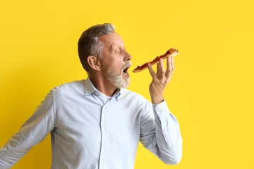 Schilderijen op glas Mature man eating tasty pizza on yellow background © Pixel-Shot