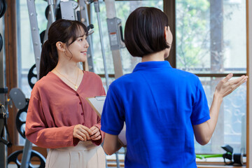 ジムでトレーナーから説明を聞く女性