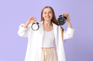 Pretty young woman with alarm clocks on lilac background