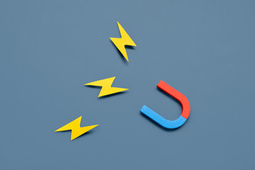Horseshoe shaped magnets with paper lightnings on blue background
