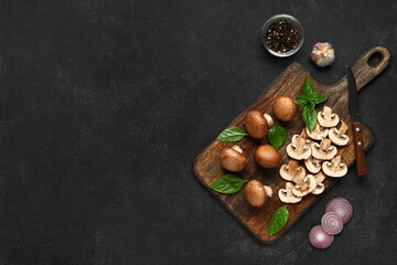 Wooden board with fresh mushrooms and different spices on black background