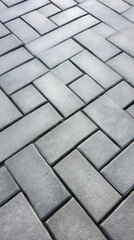 Closeup of a concrete sidewalk with small square tiles, each with a raised texture resembling a woven pattern. The tiles have a light grey color and add depth and dimension to the sidewalks