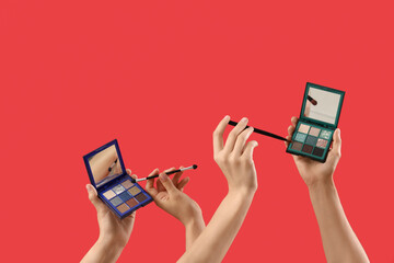 Women with eyeshadows and makeup brushes on red background