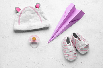 Baby hat, booties, pacifier and paper plane on light background