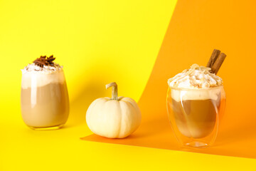 Glasses of tasty pumpkin latte with cinnamon, almond and star anise on colorful background