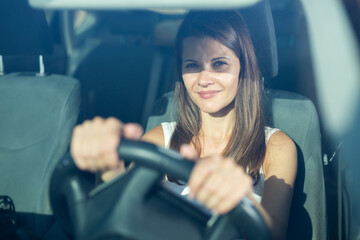 Positive young adult woman driving car during solo trip, front view