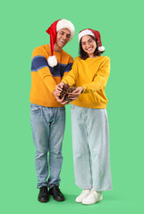Happy young couple in Santa hats with forest bumps on green background