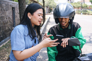 Young female customer showing destination to online motorcycle taxi driver by smartphone - obrazy, fototapety, plakaty
