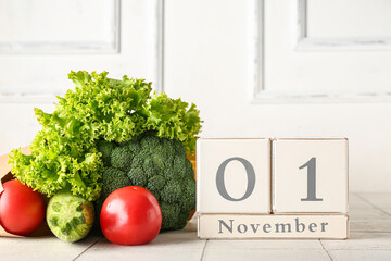 Fresh vegetables and cube calendar with date NOVEMBER 1 on table near white wooden wall. World...
