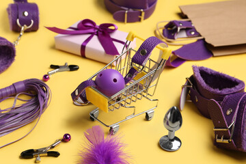 Shopping cart with sex toys on yellow background, closeup
