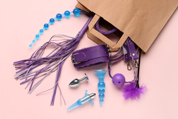 Shopping bag with different sex toys on pink background