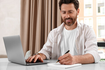 Man working on laptop and writing something at table in cafe