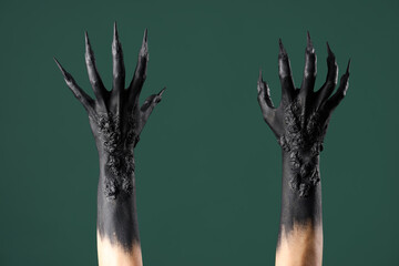 Black hands of witch with claws on green background. Halloween celebration