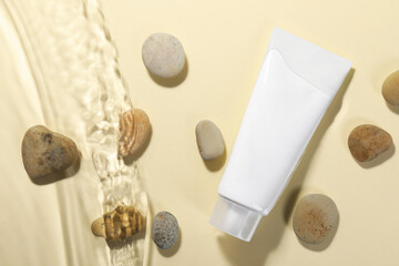 Fototapeta na wymiar Tube of face cleansing product and stones in water against beige background, flat lay