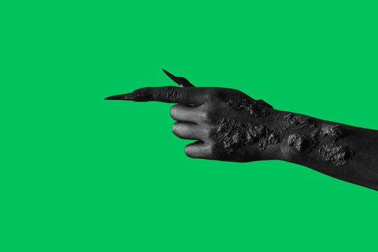 Black hand of witch pointing at something on green background. Halloween celebration