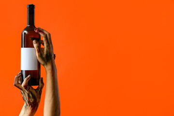 Zombie hands holding bottle of wine with blank label on orange background. Halloween celebration