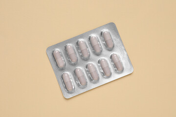 White pills in blister on beige background, top view